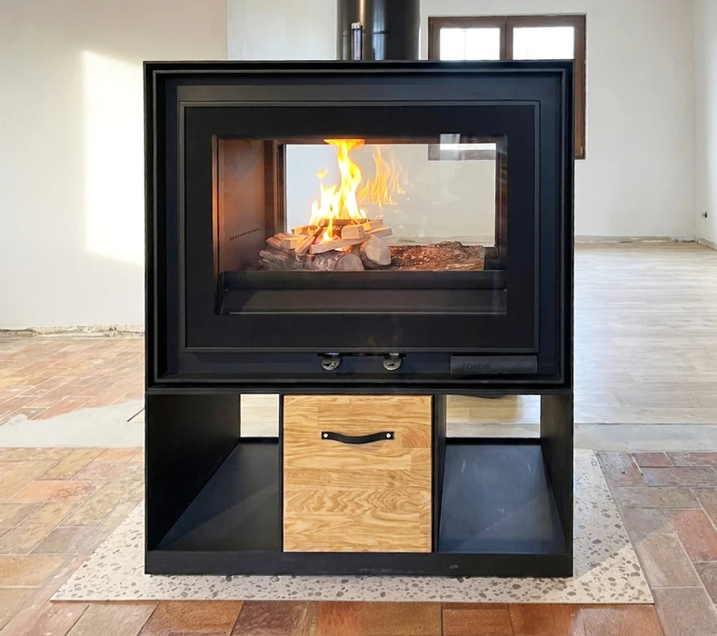 Poêle à bois design moderne **Fondis**, double face vitré, monté sur meuble bas en acier noir mat avec tiroir central en chêne massif et rangements latéraux ouverts