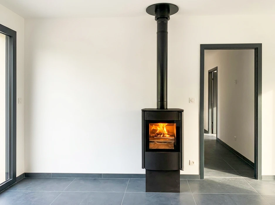 Poêle à bois design noir autonome en fonte, vitré, allumé avec flammes visibles, installé dans une pièce neuve épurée