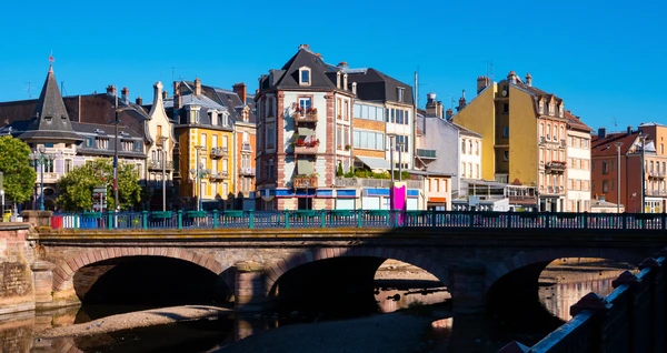 Photographie panoramique en haute résolution de la ville de Belfort et ses environs, montrant ses caractéristiques architecturales et paysagères distinctives (ses fortifications historiques ou son architecture urbaine visible depuis un point de vue surélevé), avec des maisons résidentielles, des zones de végétation et des routes typiques de cette région de Bourgogne-Franche-Comté, capturant l'essence géographique du secteur d'intervention de l'entreprise.